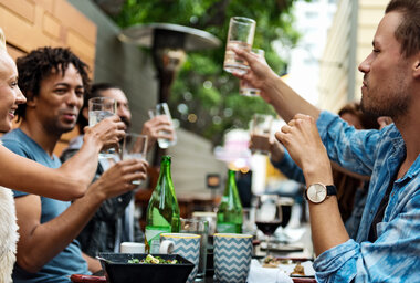 people raise their glass to toast while sitting around a table