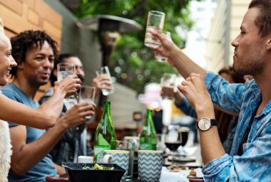 people raise their glass to toast while sitting around a table