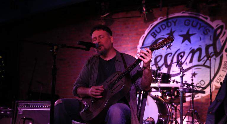 man sings into microphone while playing guitar on stage at buddy guy's