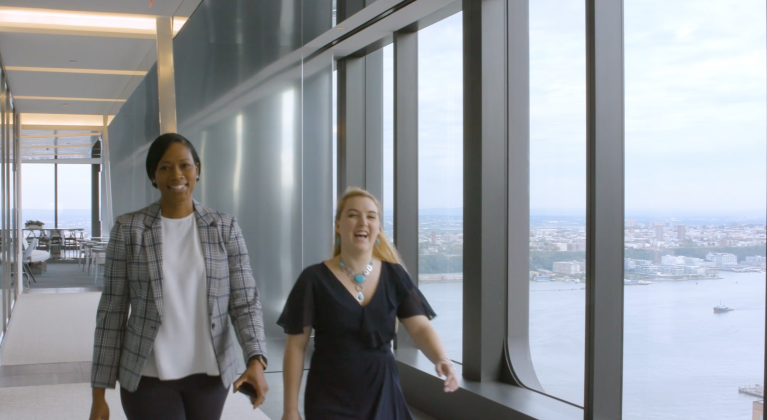 two women walk beside windows in office building